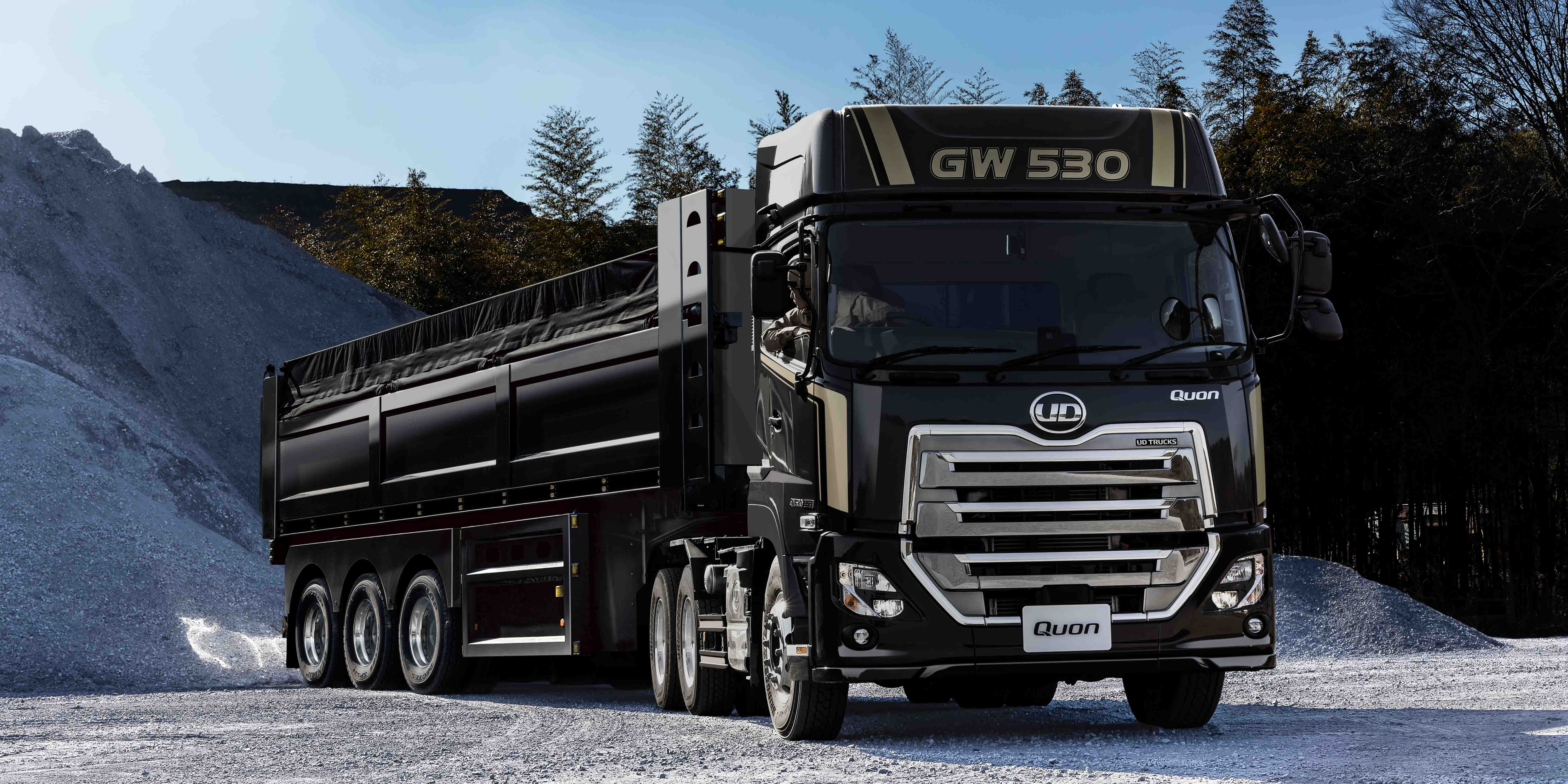 黒い大型ダンプトラックが白い砂利の山の前に停車している。