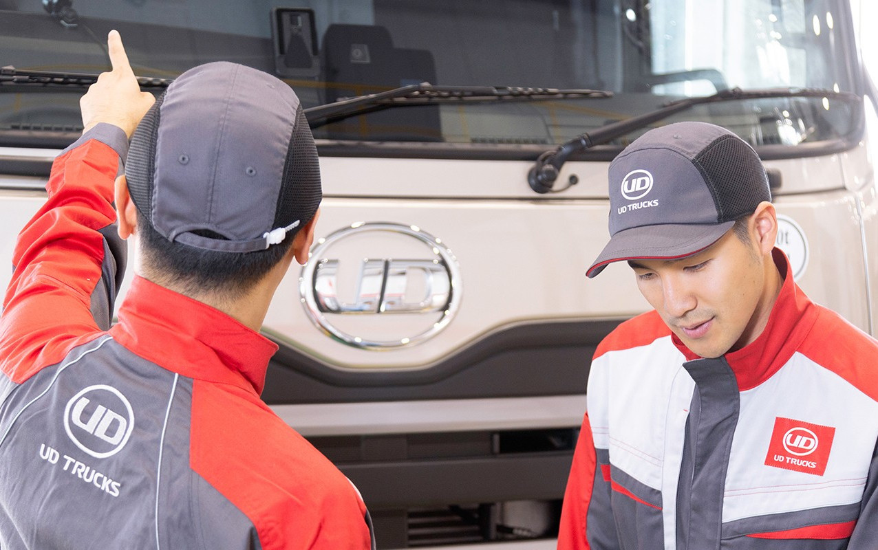 Two mechanics in red uniforms inspect a white truck.