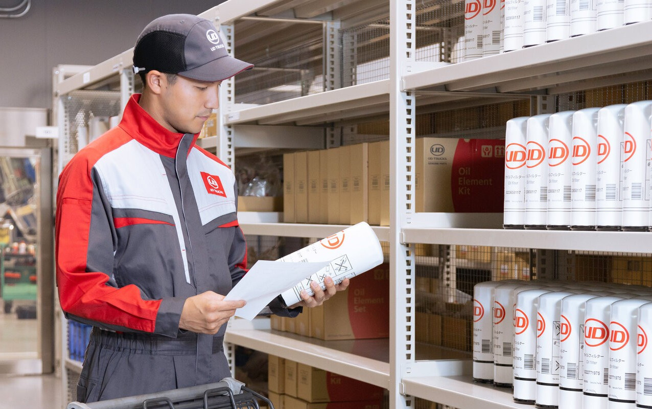 Man in uniform checks inventory in a warehouse aisle with shelves of white cans.