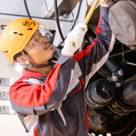 Worker in safety gear inspecting machinery with a flashlight.