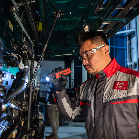 Mechanic in uniform inspects machinery with a flashlight in a workshop.