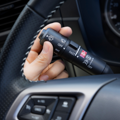 Hand turning a car wiper control lever behind a black steering wheel.