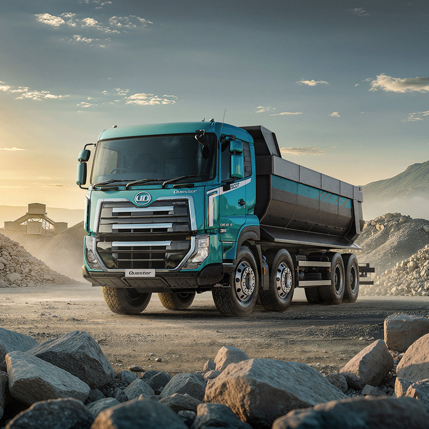 Blue dump truck on a gravel lot, surrounded by rocks and distant mountains at sunset.
