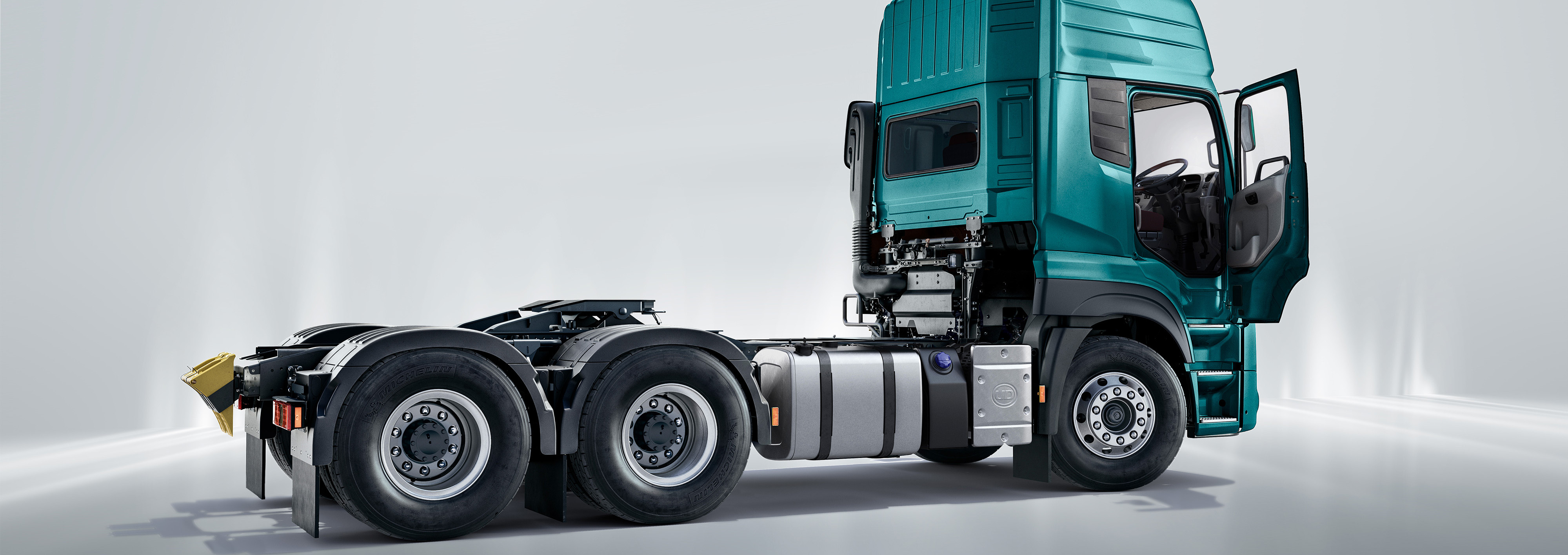 Green truck cab with open door, chassis exposed, parked indoors on a white background.