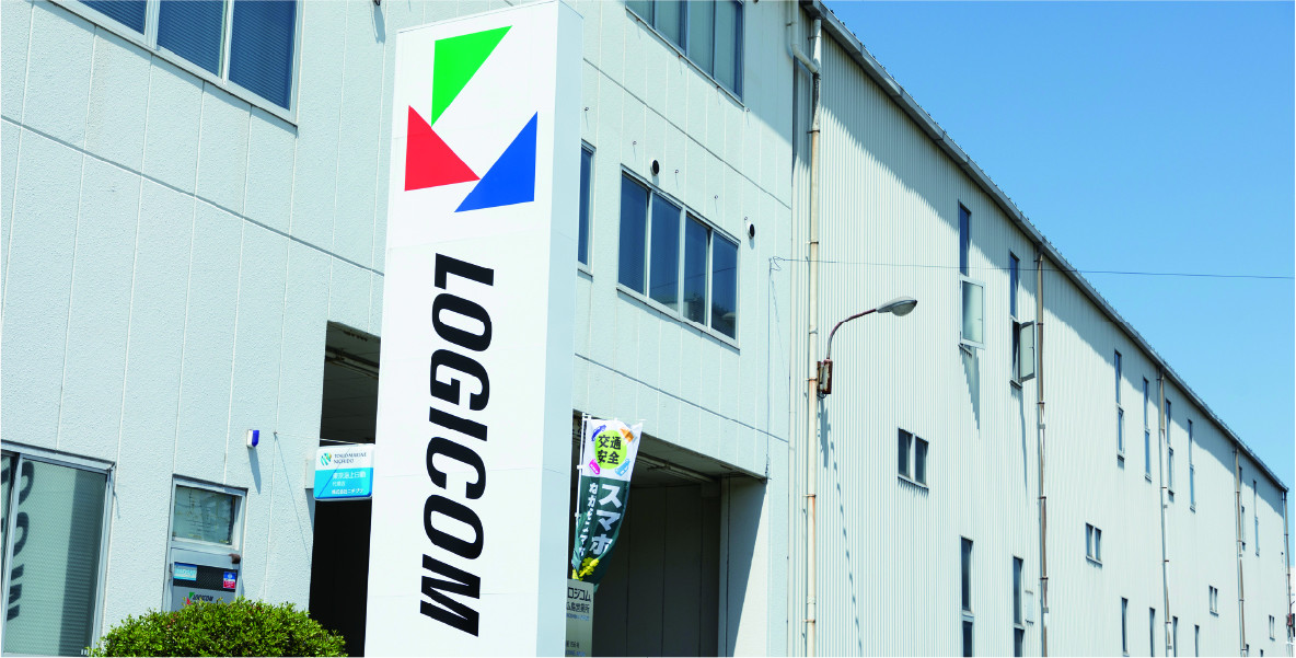 白い建物の前にLOGICOMのロゴが描かれた縦長の看板