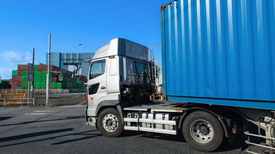 Truck hauling a blue shipping container at a freight yard under a clear sky.