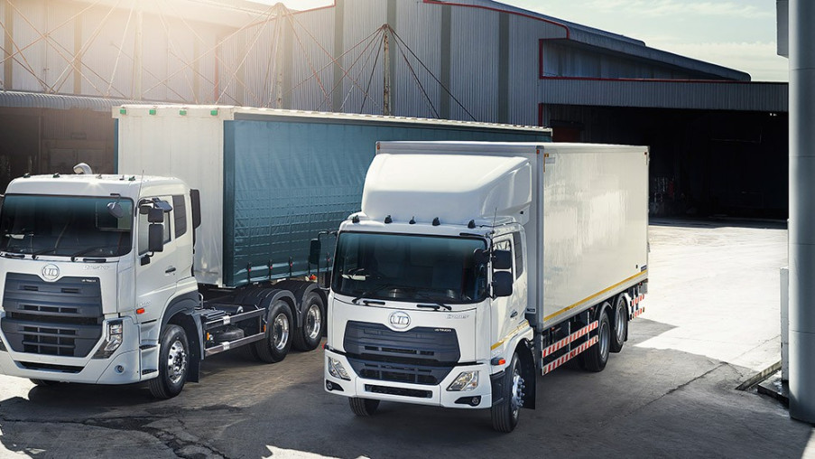 Two white cargo trucks parked outside a warehouse in daylight.