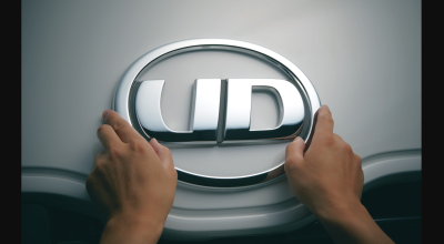 Two hands touching a silver UD logo emblem on a vehicle.