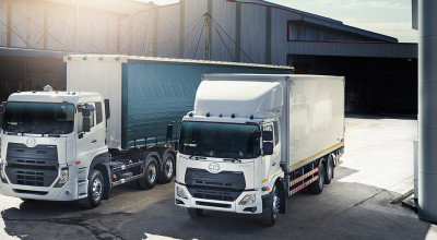 Two white cargo trucks parked outside a warehouse in daylight.