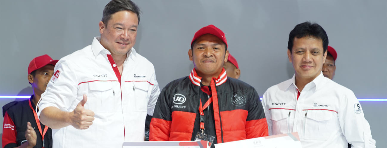 Tiga pria berpose bersama, satu mengenakan jaket hitam dan topi merah.