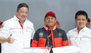 Tiga pria berpose bersama, satu mengenakan jaket hitam dan topi merah.