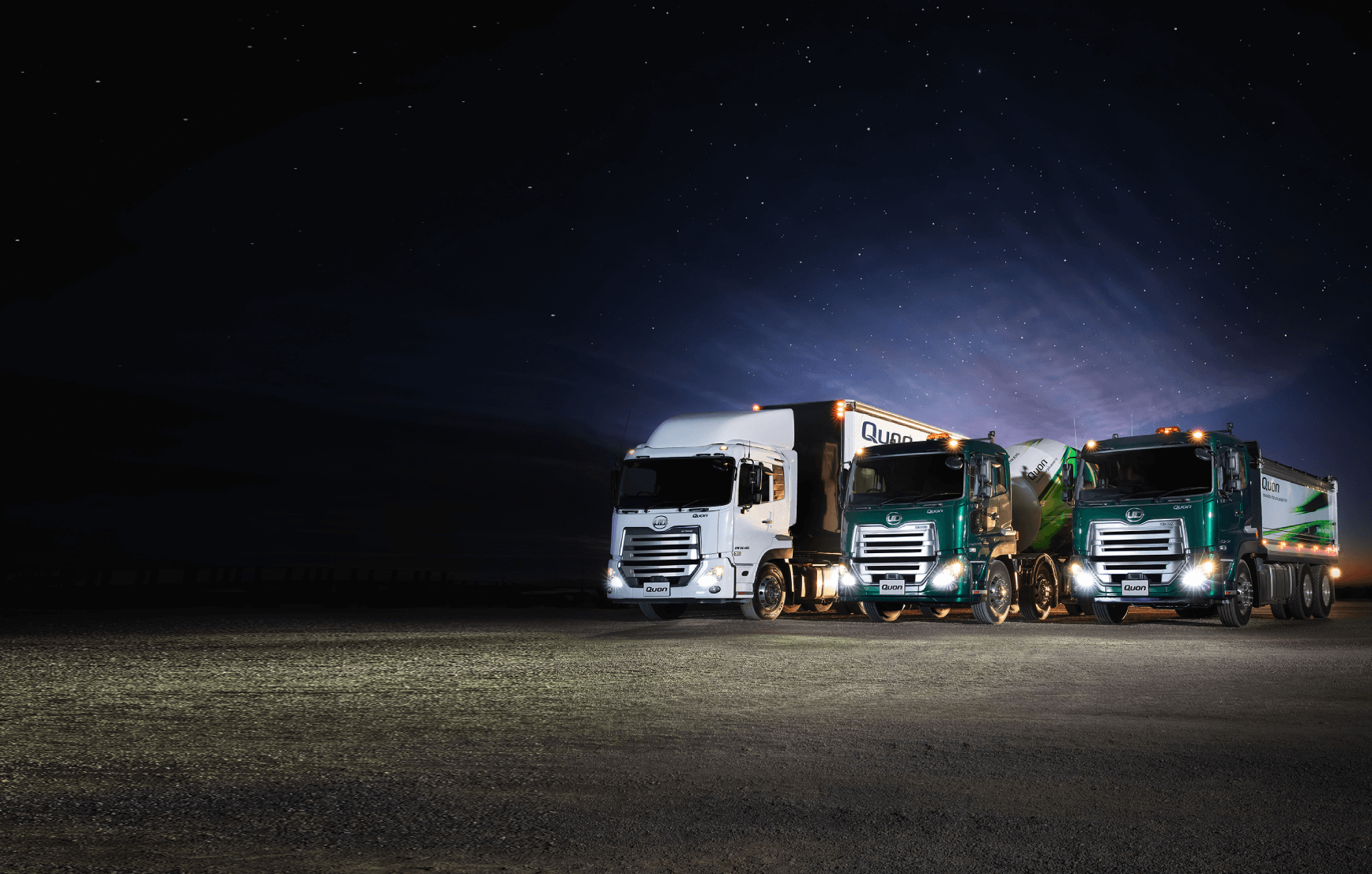 Three trucks parked side by side under a starry night sky with headlights on.
