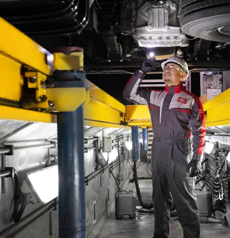 ช่างสวมชุดป้องกันตรวจสอบรถยนต์ใต้ท้องรถในอู่ซ่อม