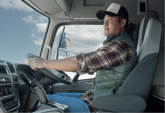 Người đàn ông đội mũ lái xe tải trong buồng lái, trời nắng nhẹ bên ngoài.