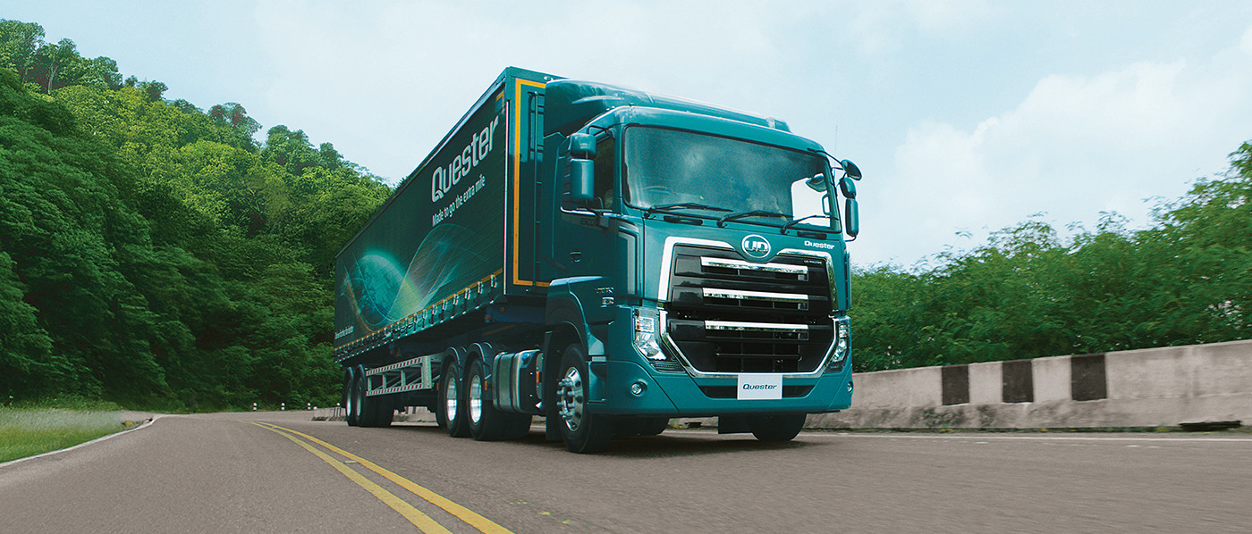 Lori ya kijani kubwa inaendesha barabarani karibu na msitu.